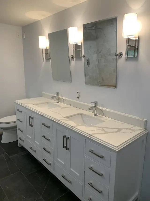Bathroom remodel with a white double vanity, quartz top, two framed mirrors with sconces and dark tile floor