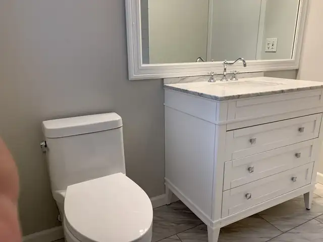 Bathroom with white furniture-style vanity, marble top, wide framed mirror and one-piece toilet