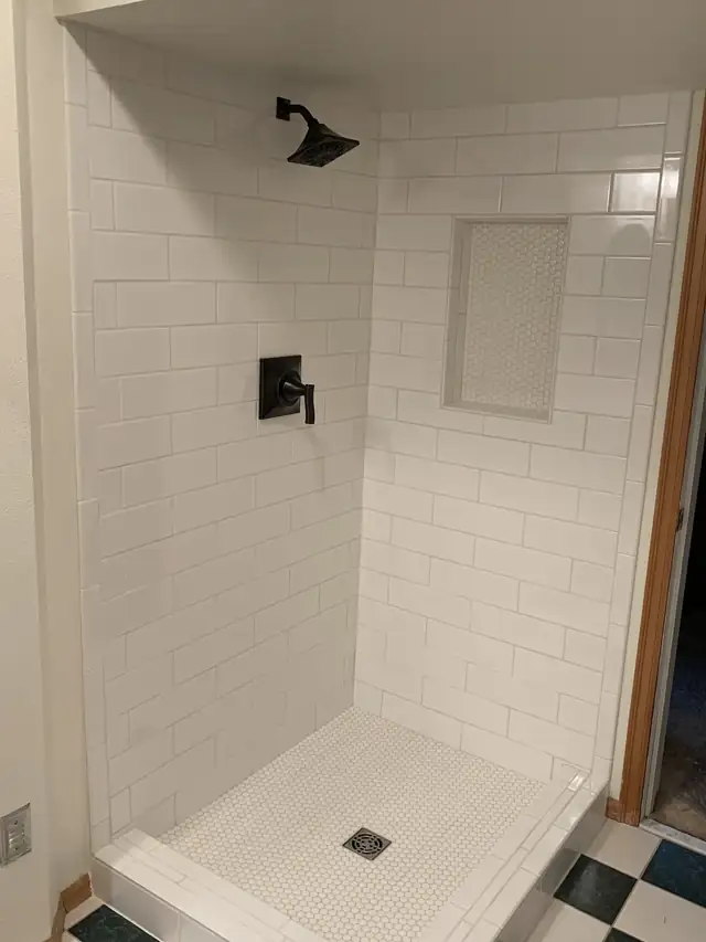 Walk-in shower with white subway tile, recessed niche, matte black fixtures and mosaic floor
