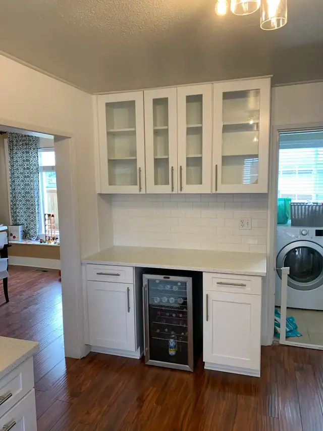 Built-in white Shaker cabinetry with glass-front uppers, a beverage fridge and a white subway tile backsplash
