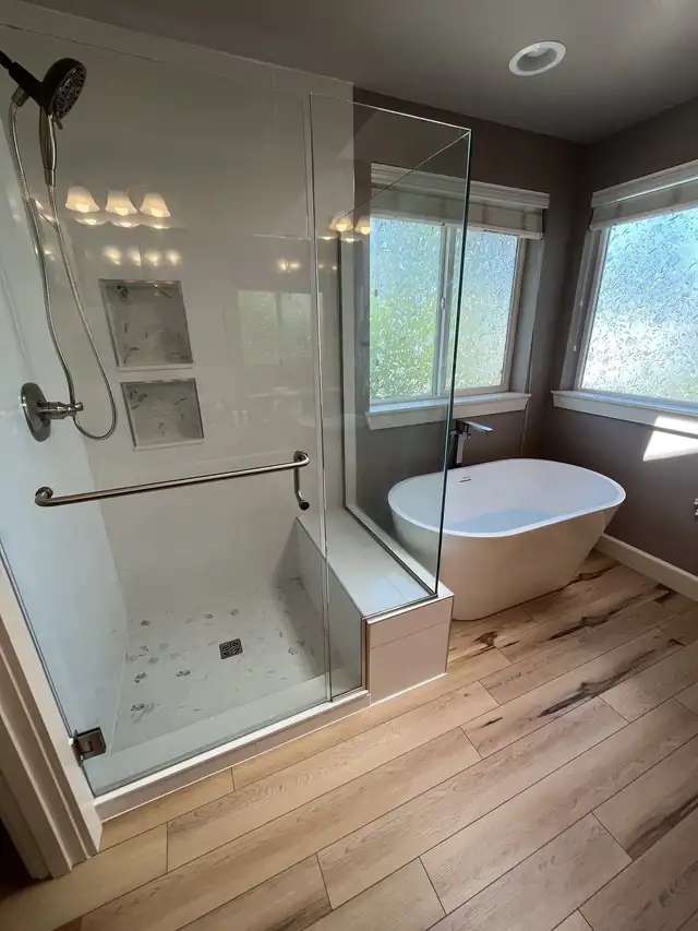 Remodeled bathroom with a frameless glass walk-in shower and bench, a freestanding tub under the windows and wood-look plank floors