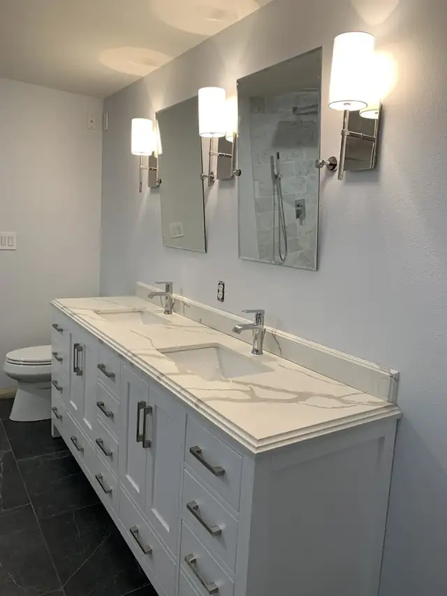 Bathroom with a white double vanity, marble-look quartz top, tall mirrors and wall sconces