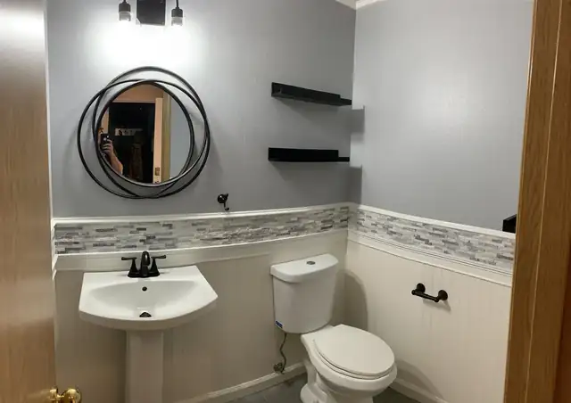 Powder room with pedestal sink, beadboard wainscot, mosaic tile band and round black mirror