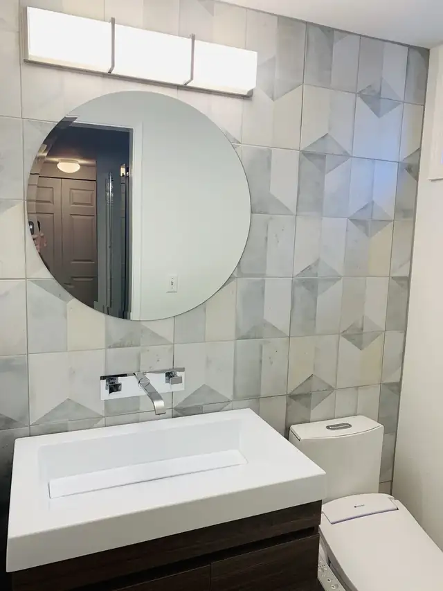 Bathroom with a floating wood vanity, white integrated sink, round mirror and geometric marble-look wall tile