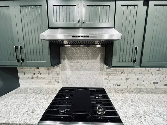 Kitchen remodel with sage green beadboard cabinets, herringbone marble backsplash, stainless hood and granite counters
