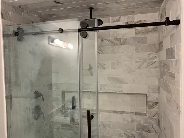 Tub-to-shower conversion with marble-look porcelain walls, recessed niche, rain head and sliding frameless glass door